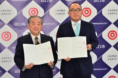 協定書を手に記念写真に納まる市川社長（右）と渡辺市長（左）