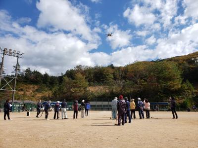 ドローンの着陸を見守るグラウンドゴルフ大会の様子