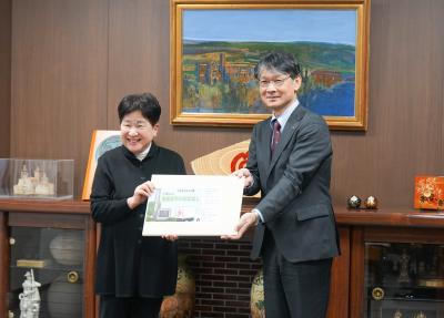 田澤代表（左）から紙芝居を受け取る市長（右）