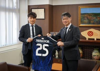 協会から本市への贈り物であるユニフォームを披露する宮本会長（左）と市長（右）