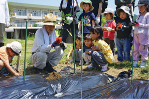 子どもたちが、地域の農家の方から、農作物の苗植えの方法を教わる様子