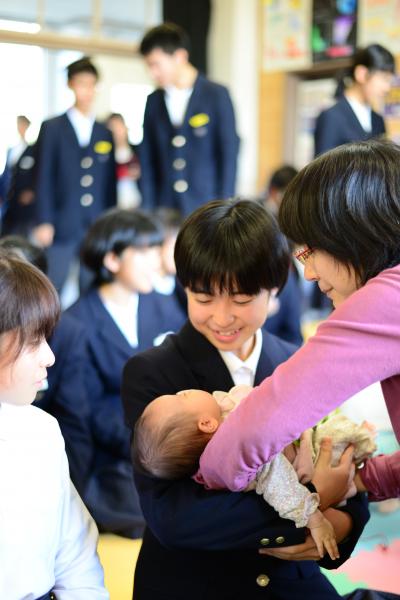 「湯田中学校ひろば」で、母親から恐る恐る赤ちゃんを受け取る湯田中学校の生徒。
