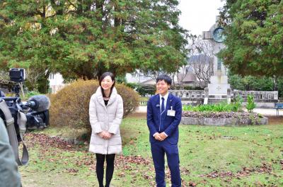 サビエル公園にて、日本ではじめてクリスマスが行われたとされる歴史について話すレポーター（左）と市の職員（右）