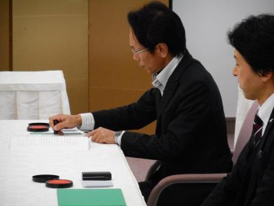 協定調印書に捺印する田中社長