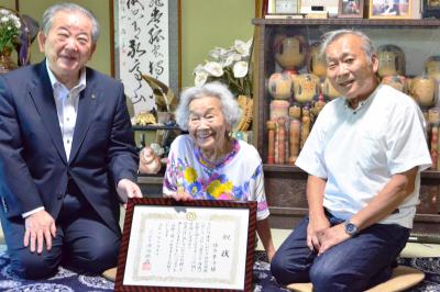 祝状を手に市長と記念撮影をする緒方幸子さん（中央）と息子さんの緒方傳治さん(右)