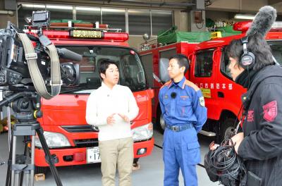 住宅用火災警報器を設置することの重要性について話すリポーター（左）と消防本部の職員（右）