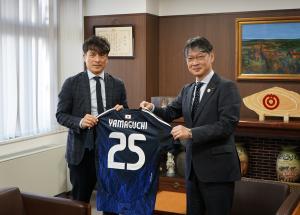 協会から本市への贈り物であるユニフォームを披露する宮本会長（左）と市長（右）